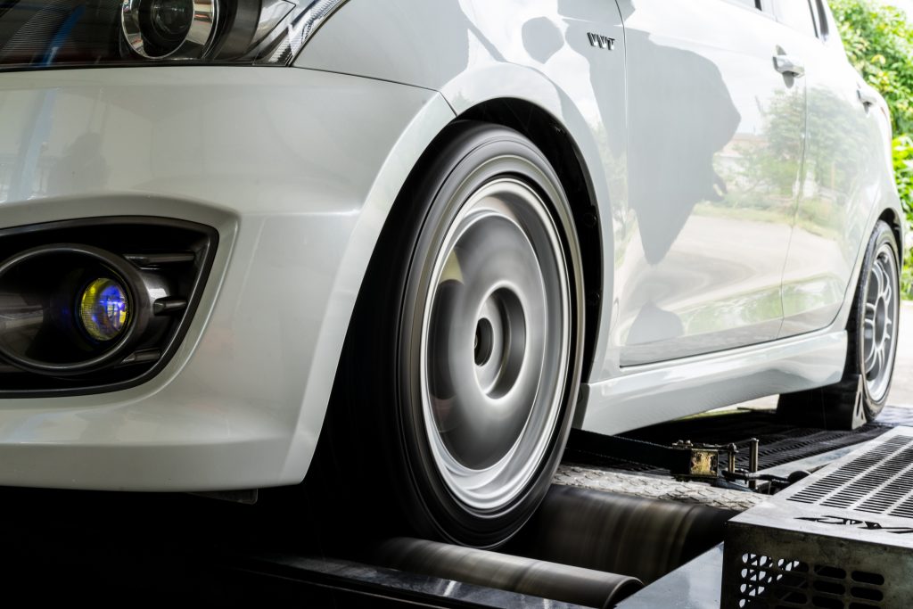 A car with front-wheel drive performs a dynamometer test in an open garage.