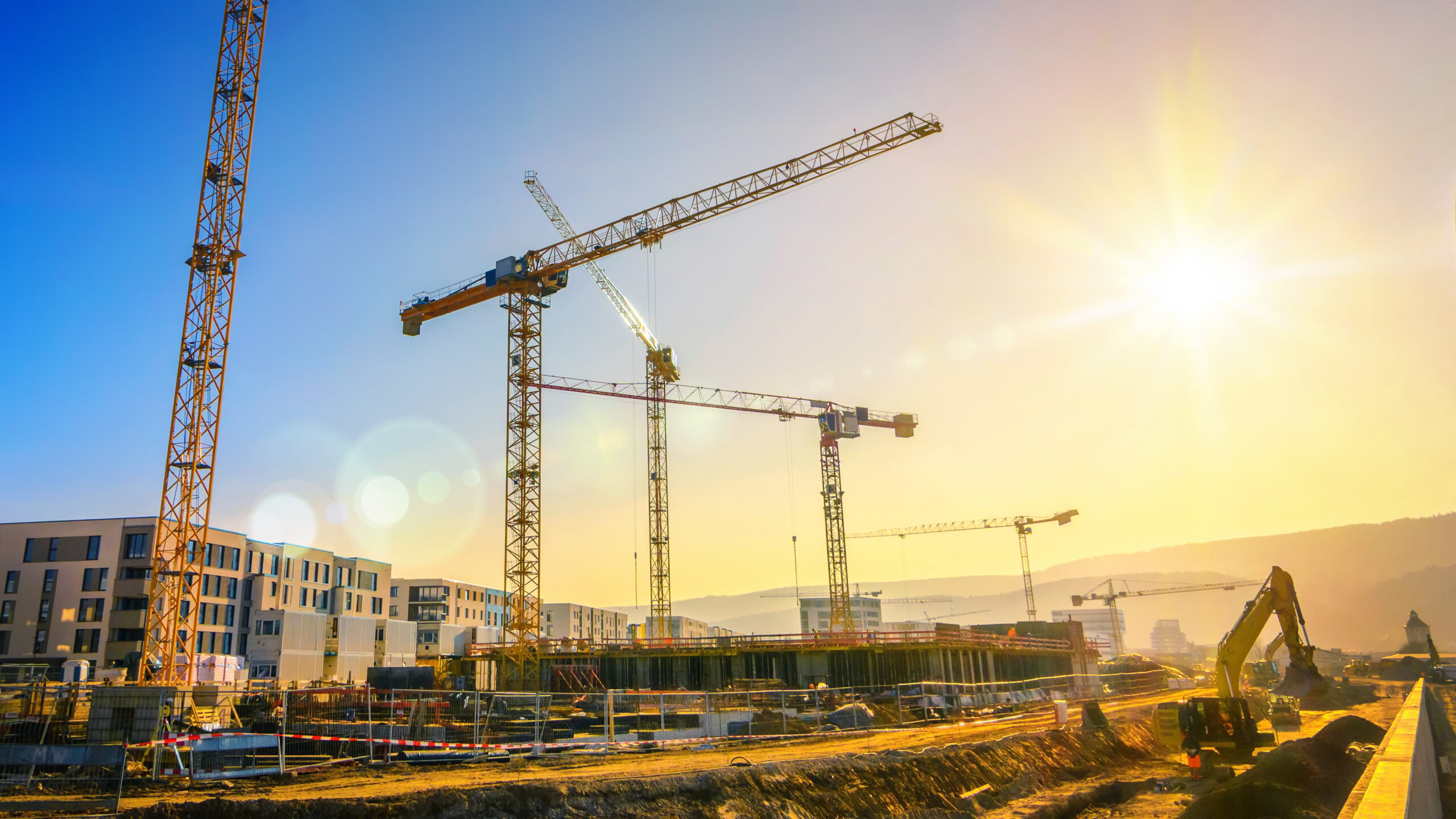 Tower cranes on a large construction site in front of a setting sun