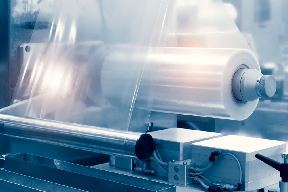 Automatic plastic bag production machine with lighting effect. Close-up of the roller of the plastic bag production machine in the light blue scene. 